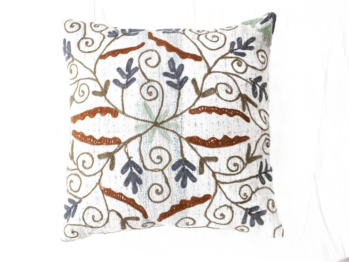 Suzani Kissenbezug in Weiß mit farbenfrohen, gestickten Schlaufenornamenten in Braun, Marineblau, Hellblau und Grün im orientalischen Bohème-Vintage-Stil.